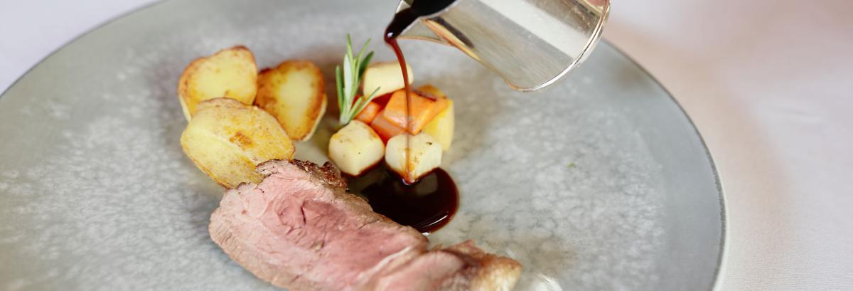 Zart rosa gebratenes Kräuterlamm mit Gemüse, Rosmarinzweig und gratiniertem Kartoffelrösti auf weißem Teller – serviert im Romantik Hotel | Restaurant Hirsch in Sonnenbühl-Erpfingen auf der Schwäbischen Alb