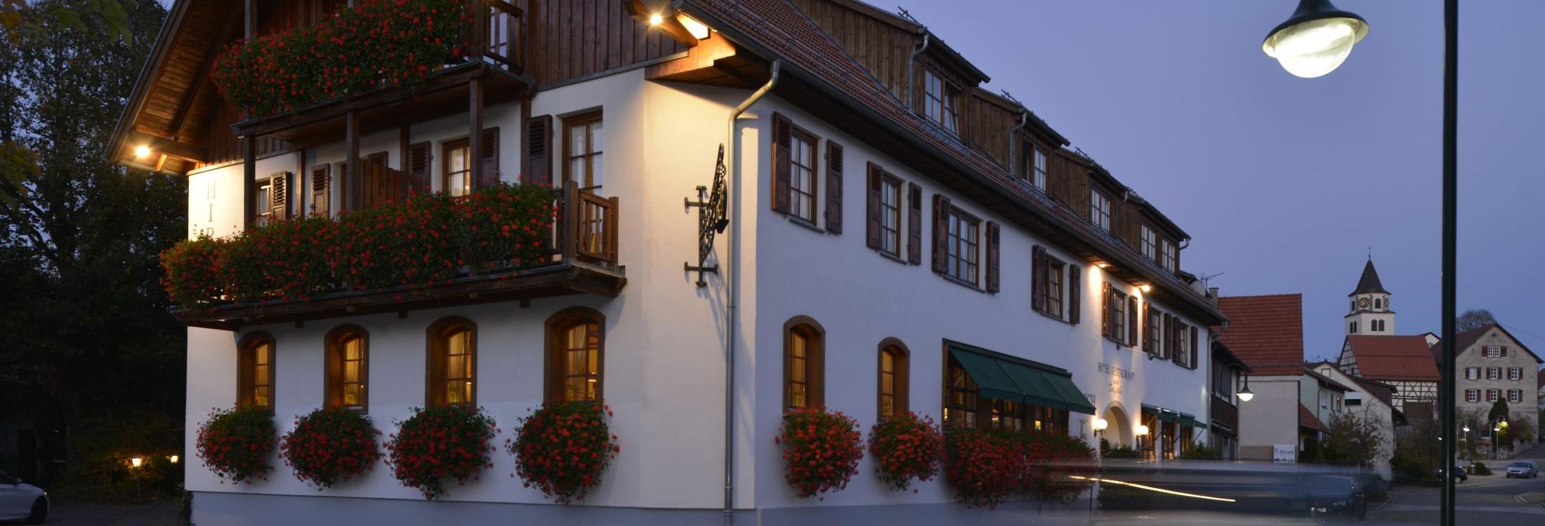 Romantik Hotel | Restaurant Hirsch in Sonnenbühl-Erpfingen am Abend mit beleuchteter Fassade und Blick auf den historischen Ortskern