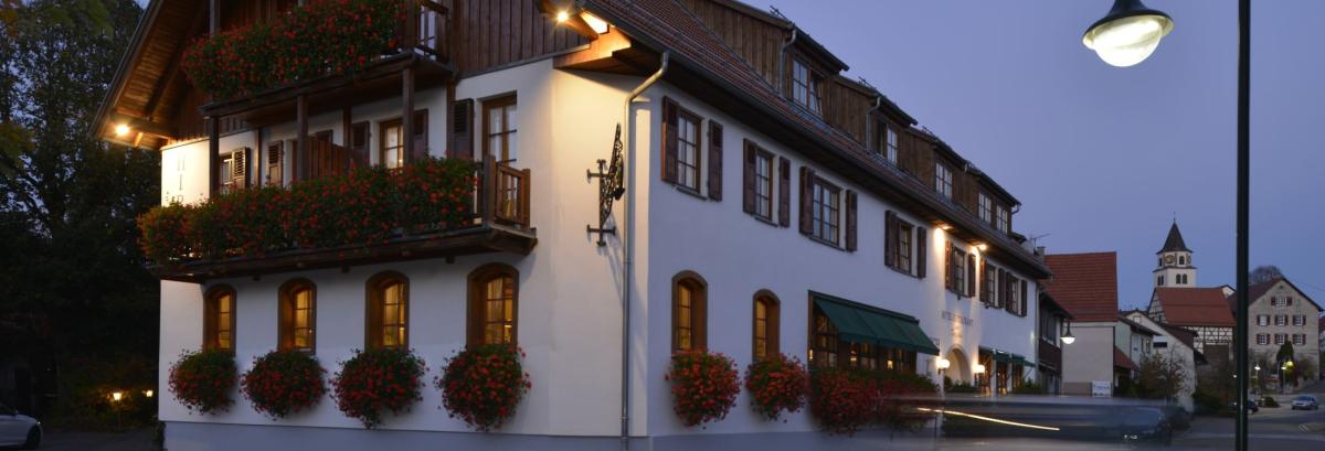 Romantik Hotel | Restaurant Hirsch in Sonnenbühl-Erpfingen am Abend mit beleuchteter Fassade und Blick auf den historischen Ortskern