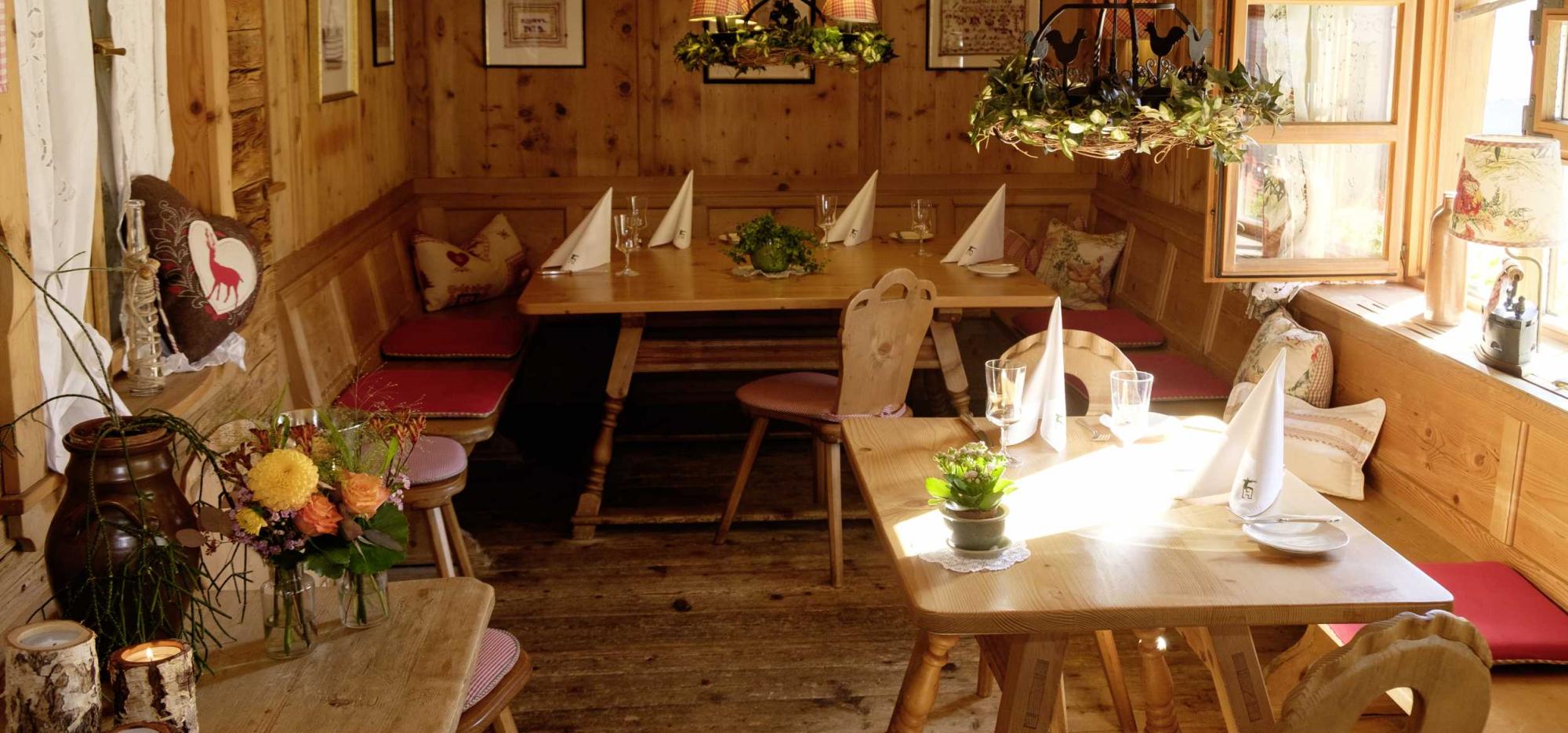 Gedeckte Tische in der Dorfstube des Romantik Hotel Hirsch, holzvertäfelte Stube mit Eckbank und Kachelofenleuchter
