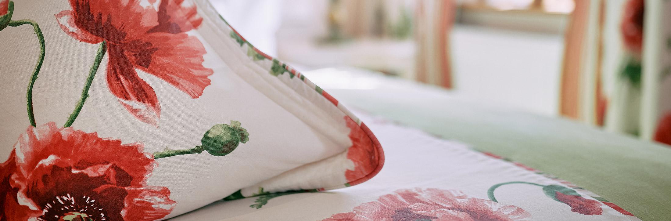 Detailaufnahme eines gemütlichen Kissens mit floralem Muster in Rot- und Rosatönen, arrangiert in einem stilvollen Gästezimmer im Romantik Hotel | Restaurant Hirsch auf der Schwäbischen Alb