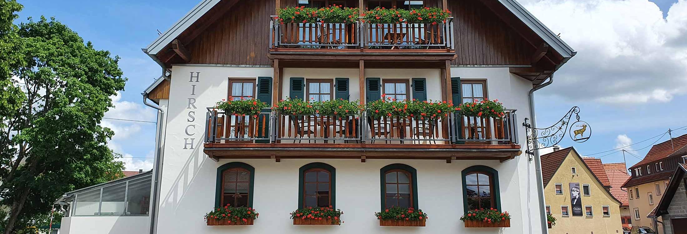 Traditionelles Gebäude mit weißer Fassade, Holzbalkonen und Blumenkästen im Romantik Hotel | Restaurant Hirsch auf der Schwäbischen Alb